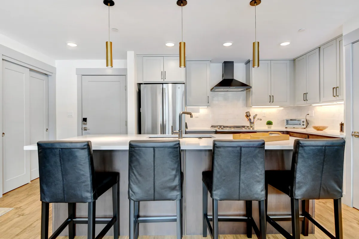 A stylish and modern gourmet kitchen featuring a spacious island with bar seating for four, pendant lights overhead, and stainless steel appliances. The layout encourages social interaction, with open sightlines perfect for entertaining or casual family meals.