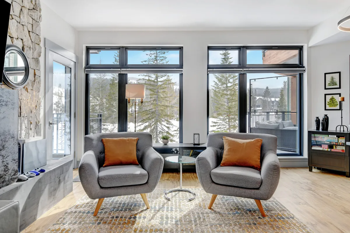 A serene sitting area with two gray armchairs accented with orange cushions, set beside large windows that reveal a snowy, wooded landscape. The cozy space invites guests to unwind, enjoy a warm drink, or read while taking in the tranquil winter scenery.