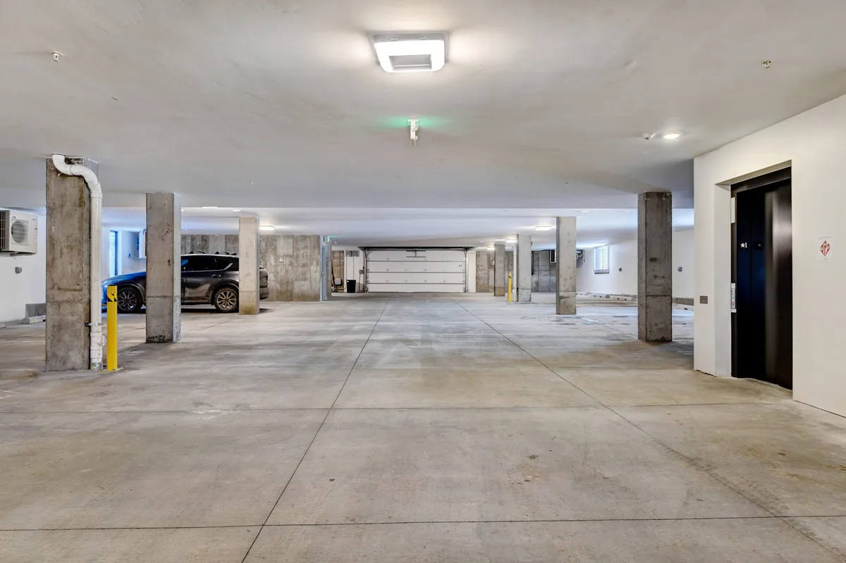 The image shows the secure, well-lit underground parking garage with organized spaces, concrete pillars, and an elevator for easy access. A car is seen parked, reinforcing the emphasis on convenience and security.
