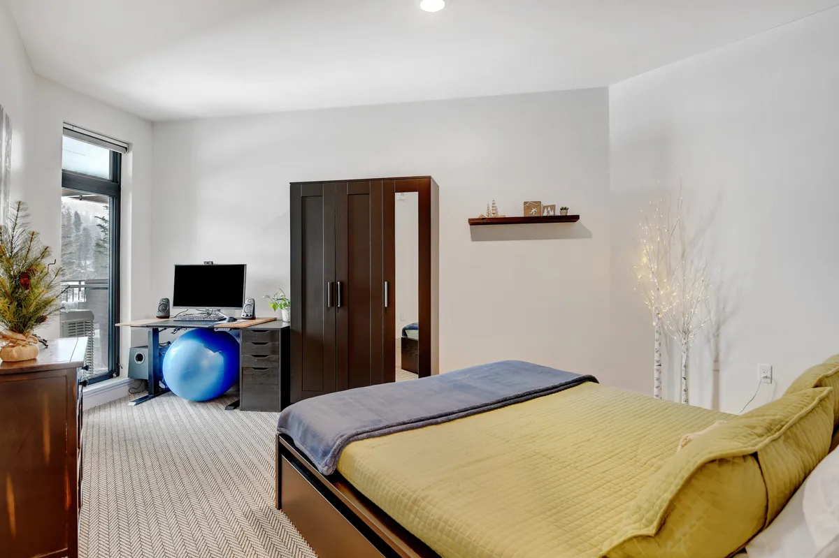 A tranquil bedroom with green and blue bedding, a desk setup with computer and an exercise ball, and a wooden dresser. The workspace is well-lit and perfectly suited for remote work, while the room remains restful and inviting.
