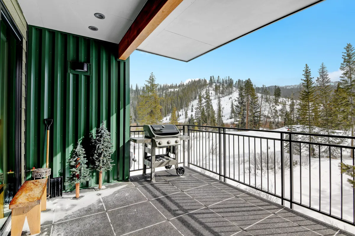 A tranquil exterior shot of a balcony overlooking a snow-covered landscape, with a grill and relaxing outdoor seating. The green wall and balcony railing create a cozy enclave, perfect for enjoying the outdoors together.