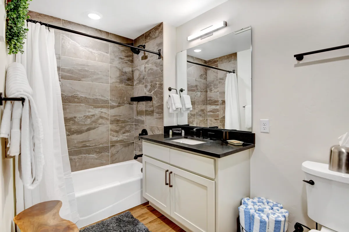 A clean, inviting bathroom featuring a bathtub, vanity, mirrored cabinet, and towel rack. The space is serene, ideal for both relaxation and convenient routines for guests or families.